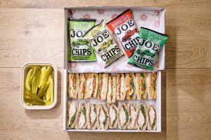 An appetizing display of freshly made sandwiches, served with a side of crunchy chips and pickles for a satisfying meal on the go.
