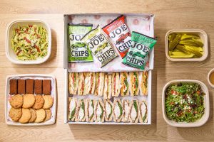 An enticing box filled with a colorful array of fresh salads, pesto salads, desserts, and a side of tangy pickles, perfect for a quick and healthy meal on the go.